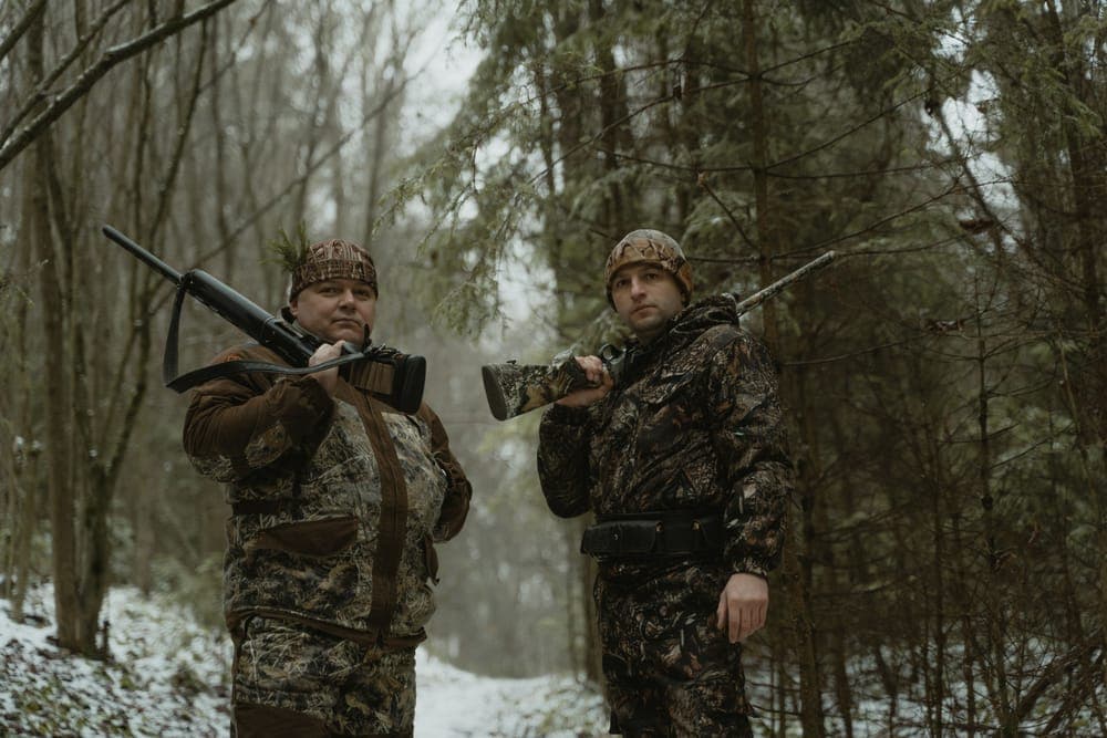 Two hunters in camouflage with rifles in a snowy forest