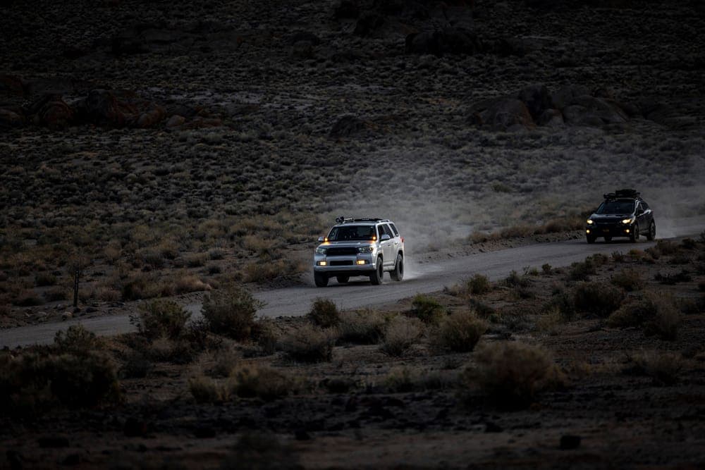 Two SUVs driving a dusty desert road at twilight