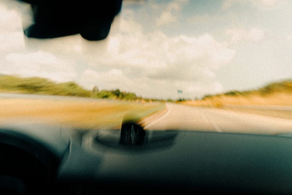 A rural road seen through a moving vehicle's windshield