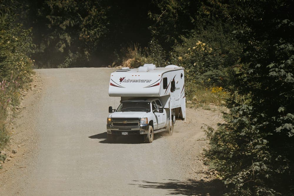 A white camper truck on a winding forest dirt road