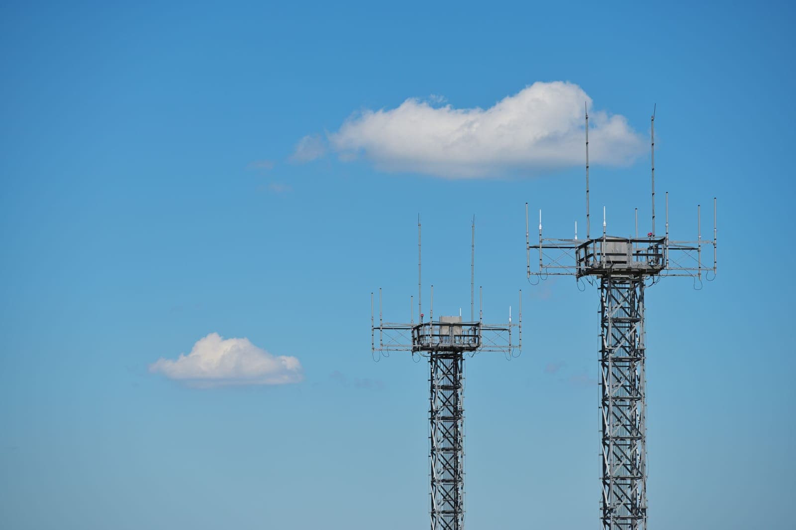 Two communication towers with antennas against a blue sky