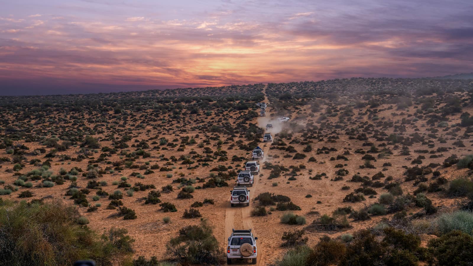 A line of vehicles crossing a desert at sunset